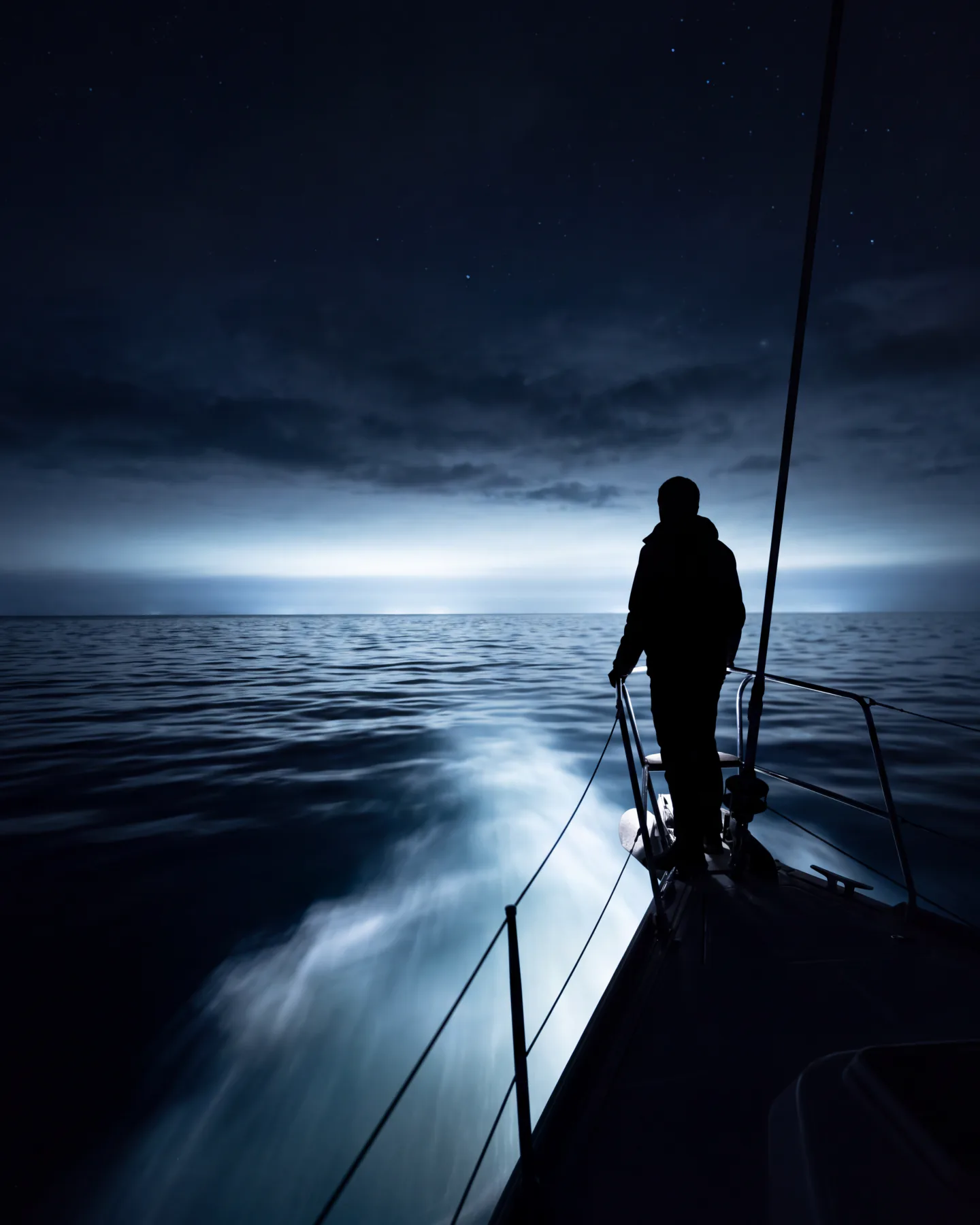 Person am Bug einer Segelyacht bei Nacht